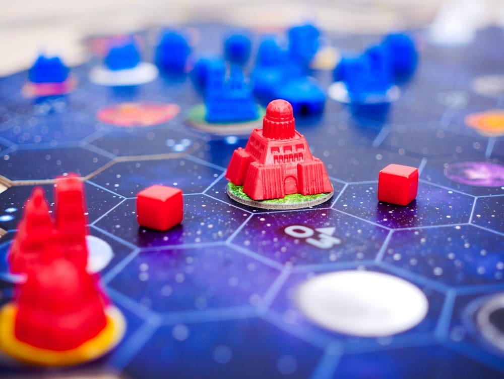 Miniaturas futuristas rojas sobre tablero hexagonal azul oscuro de Gaia Project