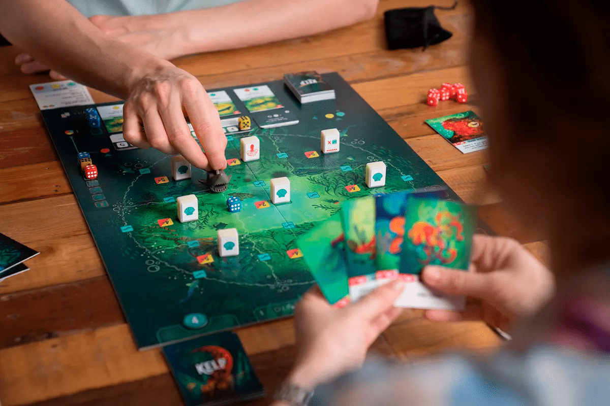 Jugadores moviendo miniatura de tiburón y cartas en partida asimétrica