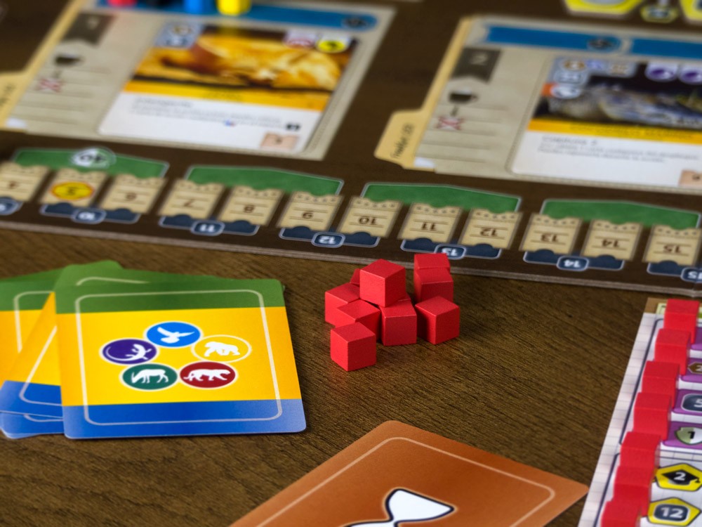 Componentes del juego de mesa Ark Nova: cartas, cubos rojos y tablero sobre madera