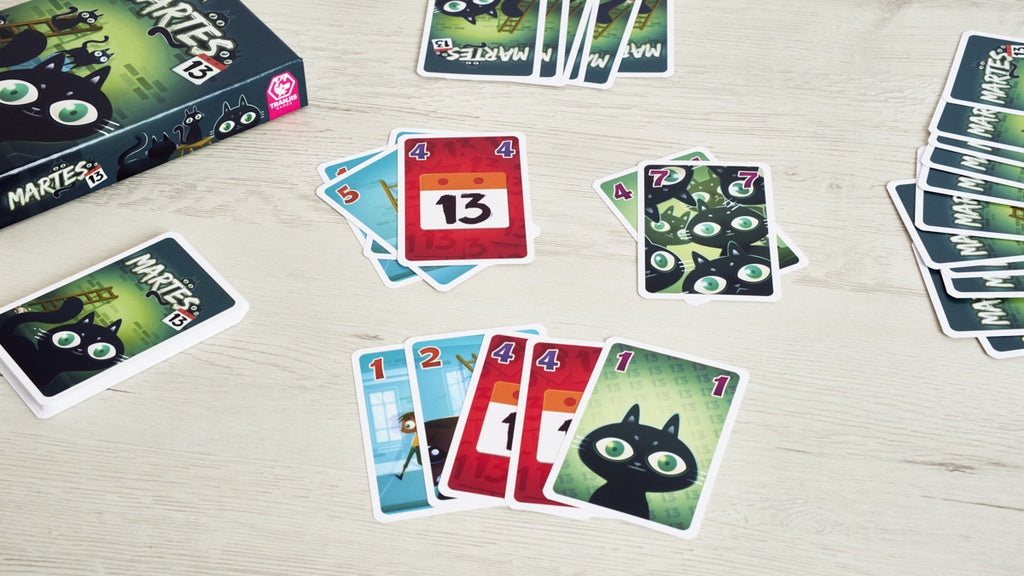 Juego de cartas Martes 13 en uso con pilas de números y carta roja del 13 sobre mesa