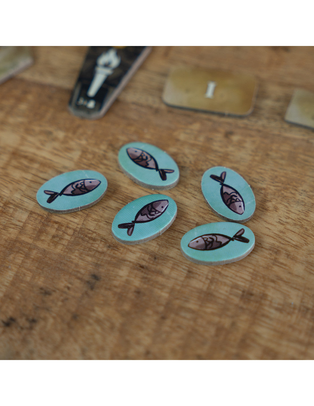 Fichas ovaladas de madera con ilustraciones de peces del juego El Pantano de Feya